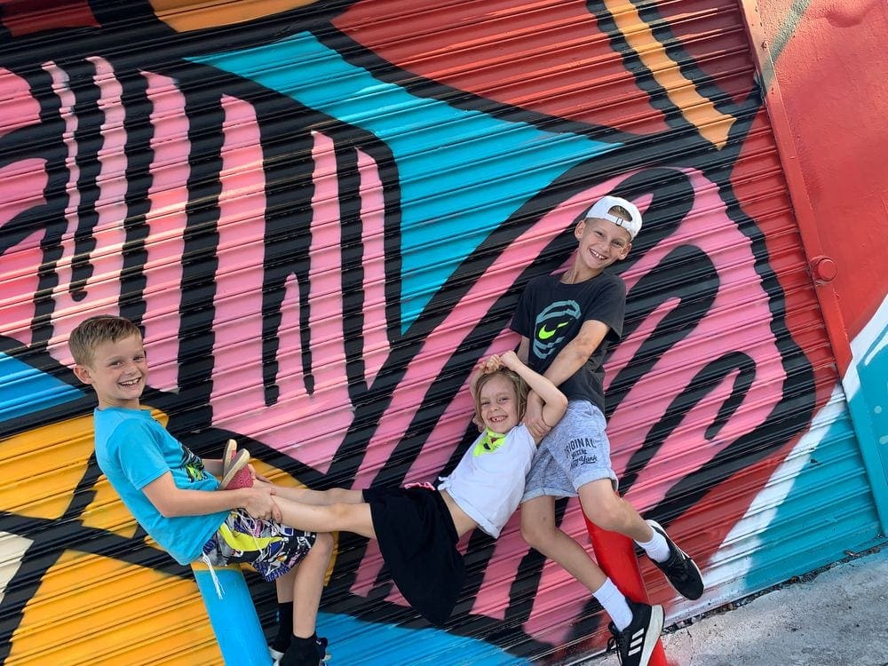 Three kids pose together in front of a colorful art installment at Wynwood Walls in Miami.