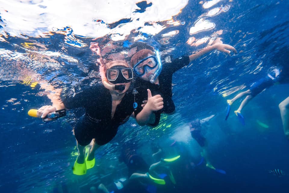 A mom and son snorkel in black wetsuits in the Great Baarrier Reef.