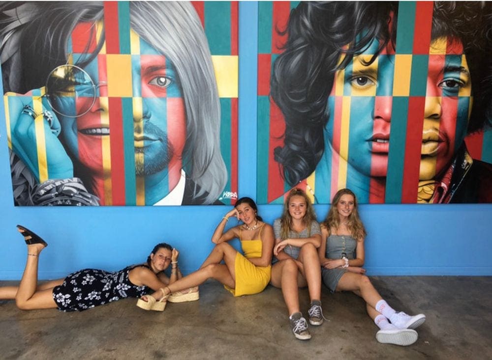 Four teenage girls pose in front of an art installment of the Beatles at Wynwood Walls.