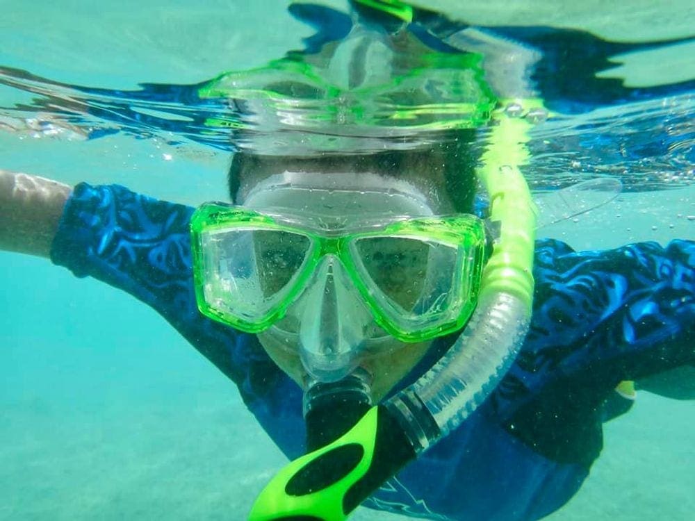 A close up of a young boy wearing lime green snorkel gear while snorkeling in Hanauma Bay, Hawaii, which is one of the best places to snorkel with kids.