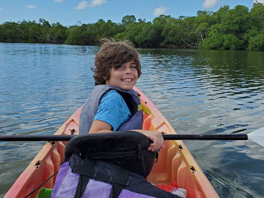 A young boy turns around while sitting in the front of a double kayak in Naples.