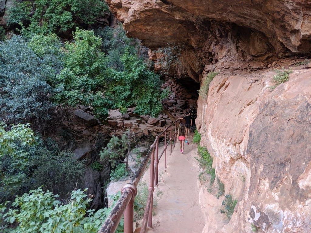 Two people walk along a narrow trail in a Utah National Park.