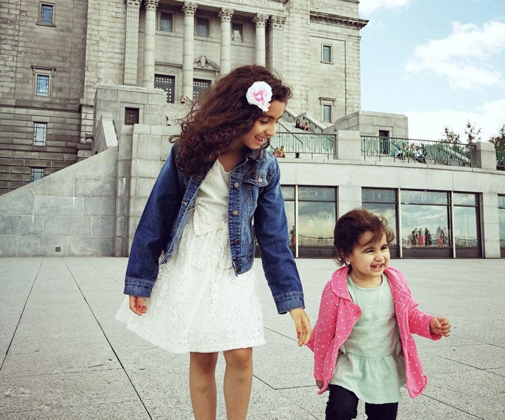 Pre-teen and toddler girls holding hands and waking around a large Canadian city.