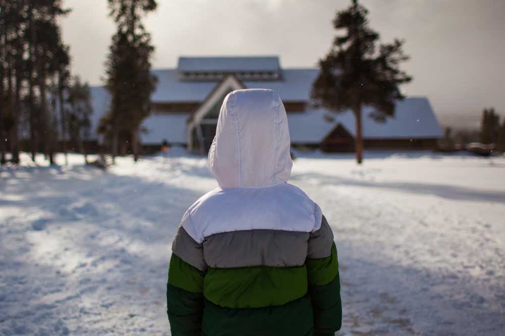 Child in winter jacket standing in show outside Old Faithful Lodge in Yellowstone