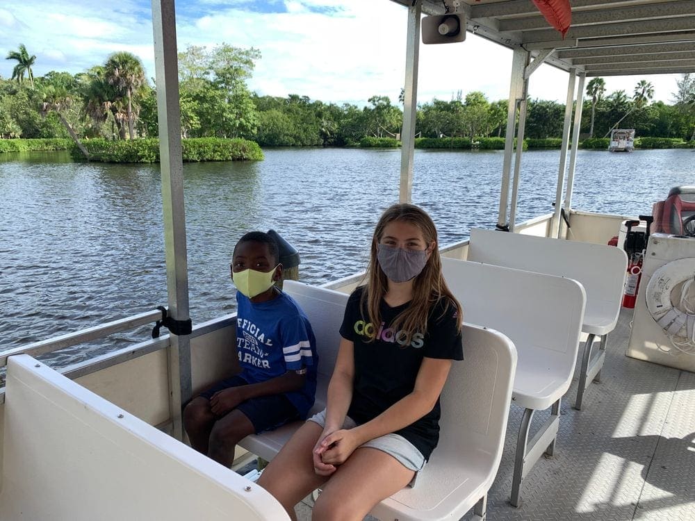 Two kids sit in a boat while enjoying a tour on the water at the Naples Zoo.