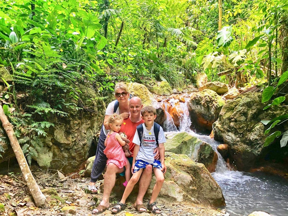 A beautiful family poses on rocks among lush foliage in Saint Lucia.