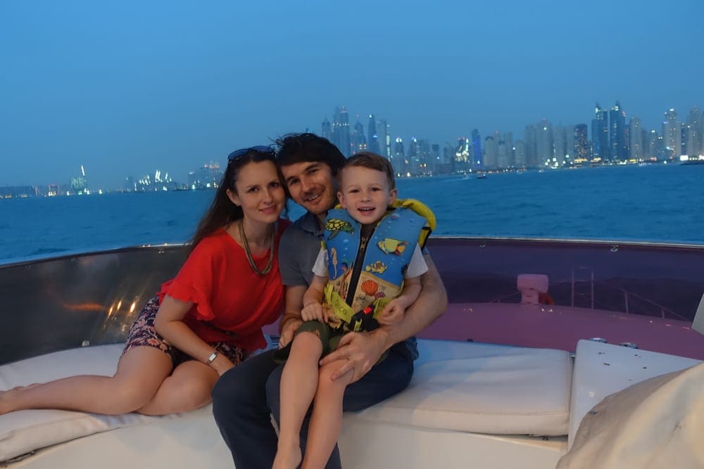 Two parents snuggle with their toddler while enjoying a boat tour in the marina in Dubai, one of the best things to do in the UAE with kids.