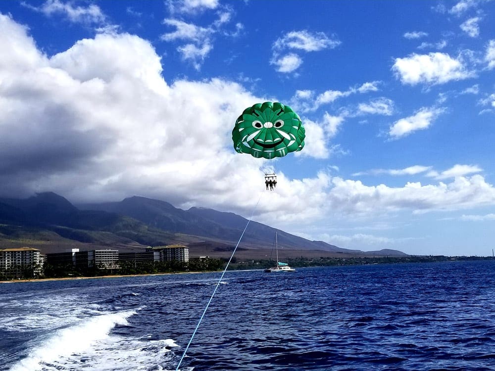 A green parasail floats in the sky above the water off the coast of Maui.