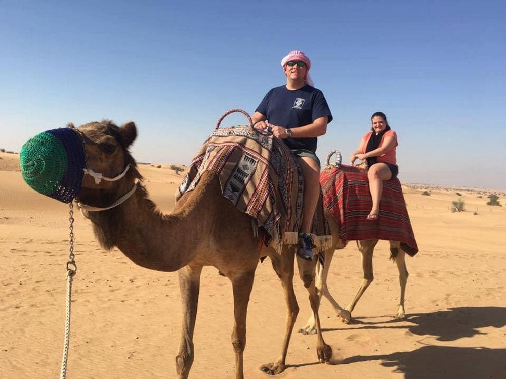 A man and woman ride their own camels on a desert tour in Dubai, one of the best things to do in the UAE with kids.