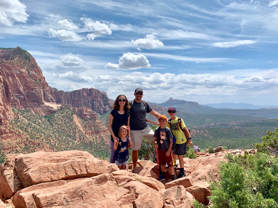 A family of five stands along a cliff with a sweeping view of Zion National Park behind them.