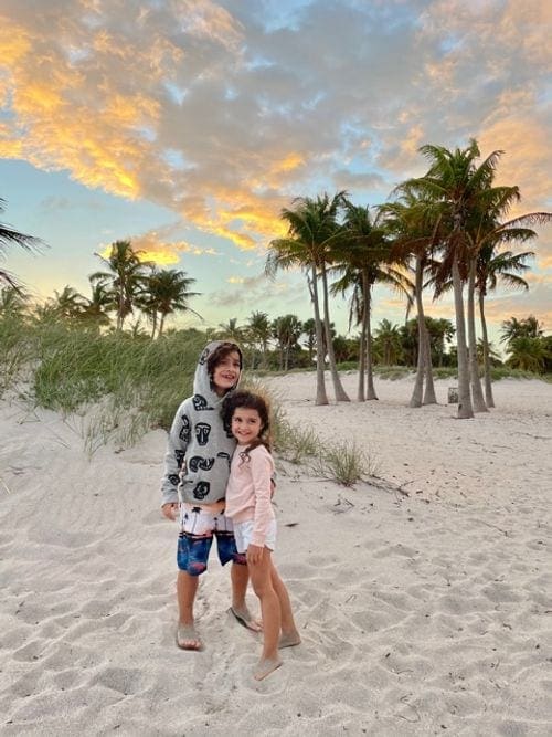 Two kids pose together on the sand in Key Biscayne at sunset.