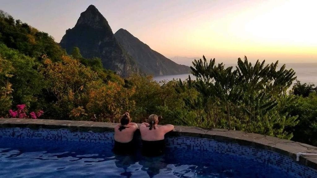 Two women in a pool look over the edge to enjoy a sunset over the Pitons in St. Lucia.