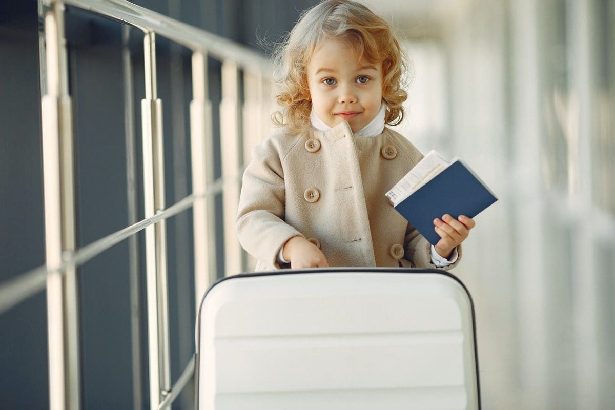 A young girl stands on the jet bridge with her suitcase and travel documents.