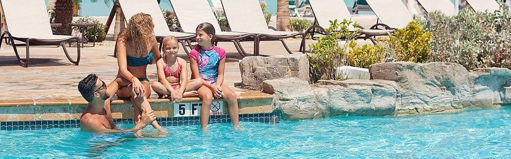 A family of four chats pool-side at Holiday Inn Aruba - Beach Resort & Casino on a sunny day.