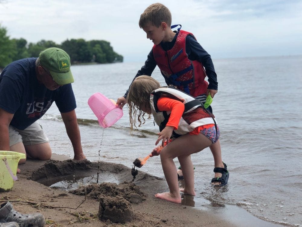 A grandpa and two kids play in the sand at Lake Mill Lacs, one of the best lakes in the Midwest for families.