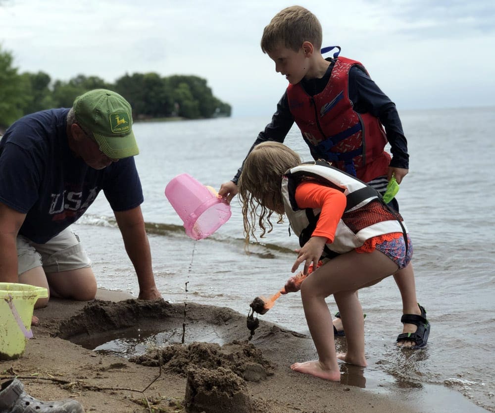 A grandpa and two kids play in the sand at Lake Mill Lacs.