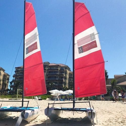 Two sail boats with red sails rest on the beach at Grace Bay Club.