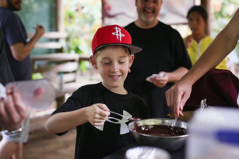 A young boy dips a spoon into fresh made chocolate on a tour in Costa Rica.