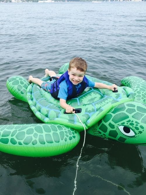 A toddler boy smiles as he rides on an inflatable turtle on Lake Wawasee, one of the best lakes in the Midwest for families.