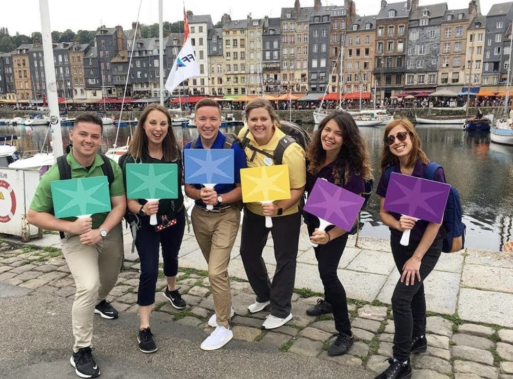 Six people hold colorfun signs in front of the Seine River while on an Adventures by Diseny tour.