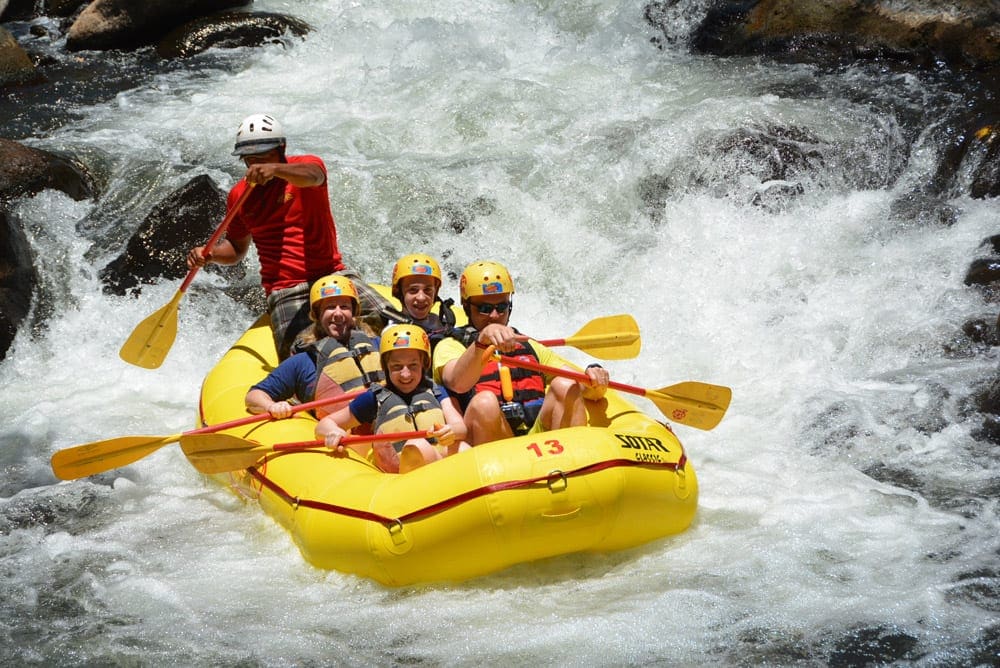 A yellow raft going down a Costa Rica river, carrying four passangers and a guide while on an Adventures by Disney tour.