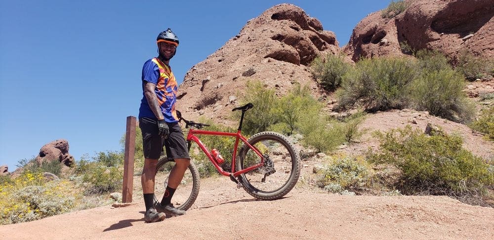 A man stands with his bike on a desert trail in Papago.