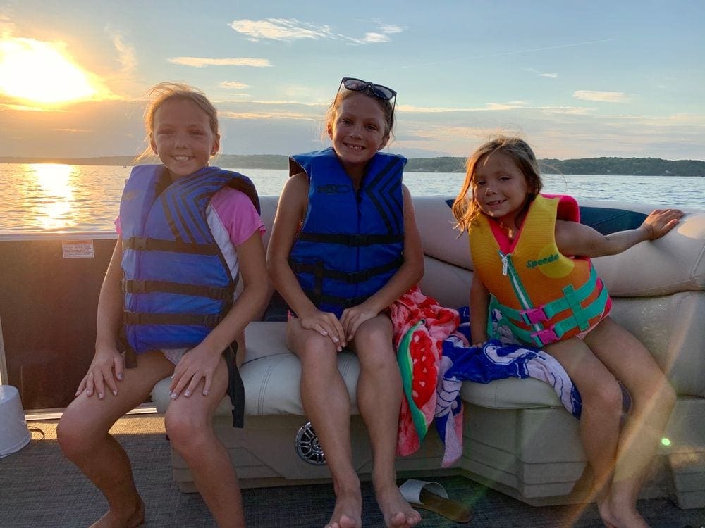 Three kids sit on a pontoon on Lake Geneva, one of the best lakes in the Midwest for families, at sunset.