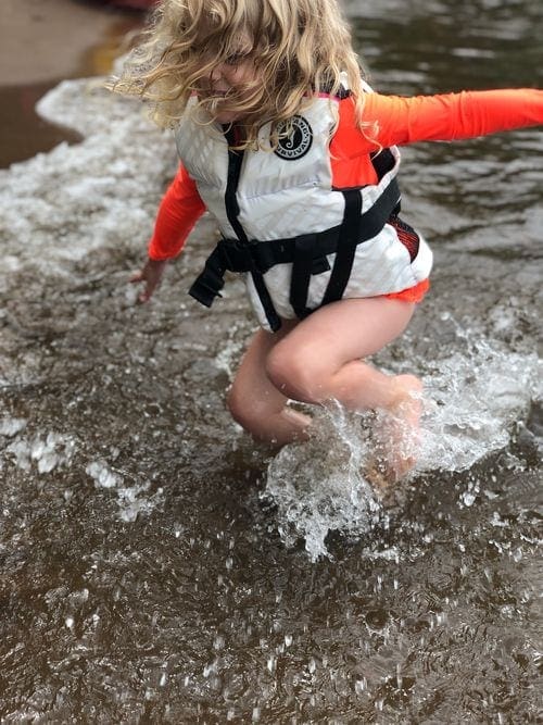 A young girl splashing along the shore of Lake Mille Lacs, while wearing a white life jacket.