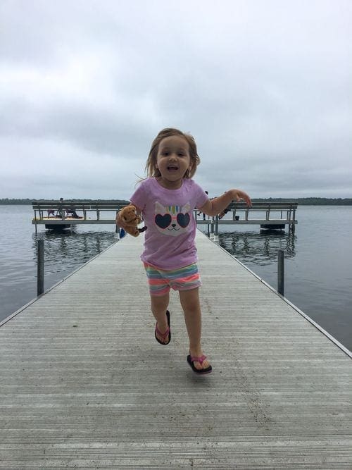 A young toddler girl runs down a dock with Leech Lake in the background.