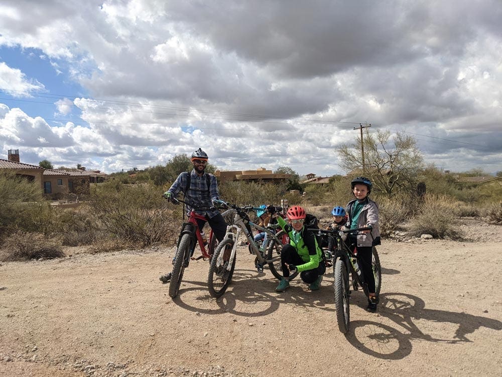 Two parents and their three kids stand among their bikes while cycling in the Arizona desert, one of the best things to do in Phoenix with kids!