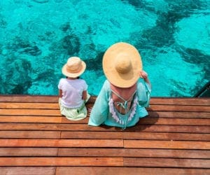 Mom and daughter sitting on a wooden platform of their over water bungalow watching the beautiful Maldives water