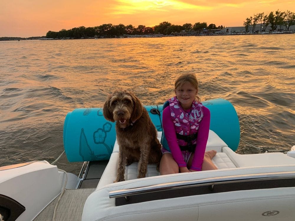 A young girl and her dog sit at the back of a boat on Lake Okoboji at sunset, one of the best weekend getaways from Minneapolis for families.