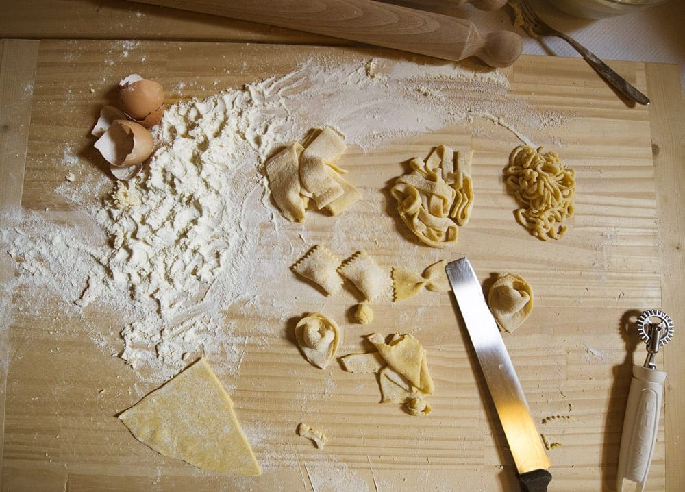 A view of a broken egg, flour, and several pasta shapes. Pasta making is available on some Adventures by Disney tours.