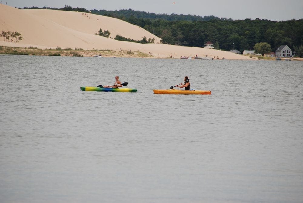 Two kayakers enjoy a nice day at Silver Lake, one of the best lakes in Michigan for a family vacation, with the iconic sand dunes in the background.