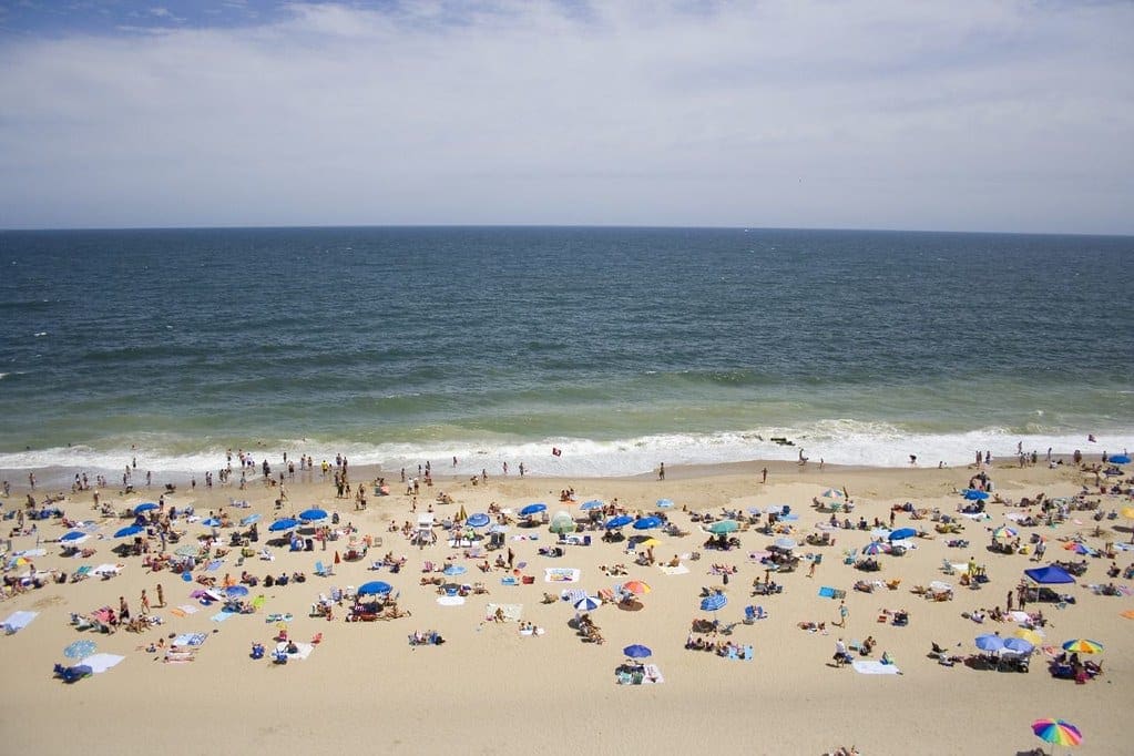 Rehoboth Beach filled with visitors and beach umbrellas on a sunny day at one of the best affordable summer vacations in the United States with kids.