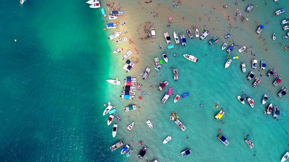 An aerial view of Torch Lake, one of the best lakes in the Midwest for families, featuring it's green-blue waters and several boats.