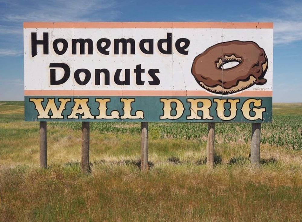 A billboard reads "Homemade Donuts, Wall Drug" on a grassy plain.
