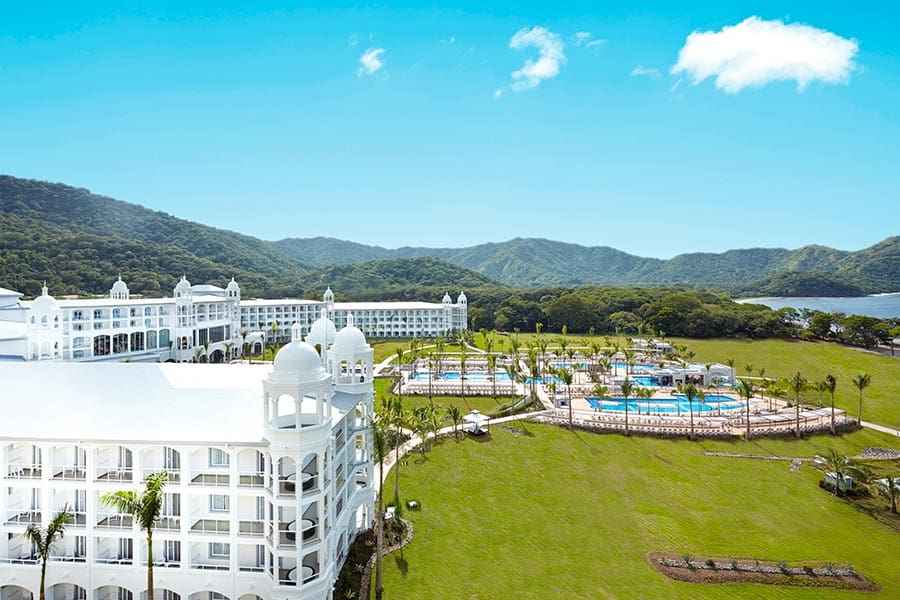 An arieal view of the pristine white hotel buildings and grassy lawn at the Hotel Riu Palace Costa Rica, one of the best Costa Rica resorts for a family vacation.