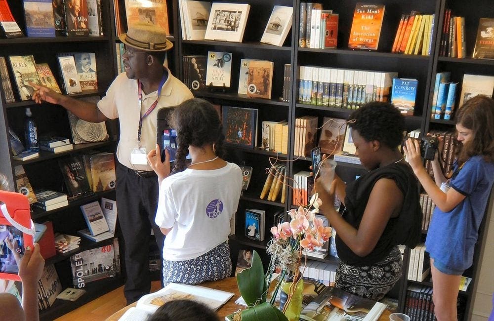 A Black man give a tour of Buxton Books to three travelers.