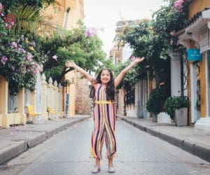 A young girl holds her hands up high in celebration of exploring beautiful Cartagena, Colombia.