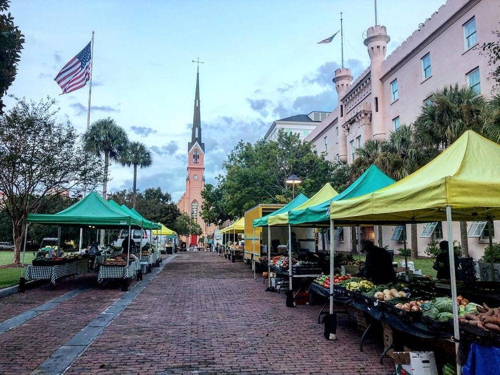 Looking down a line of vendors on each side of a cobblestone streets for the Charleston Farmers Market.