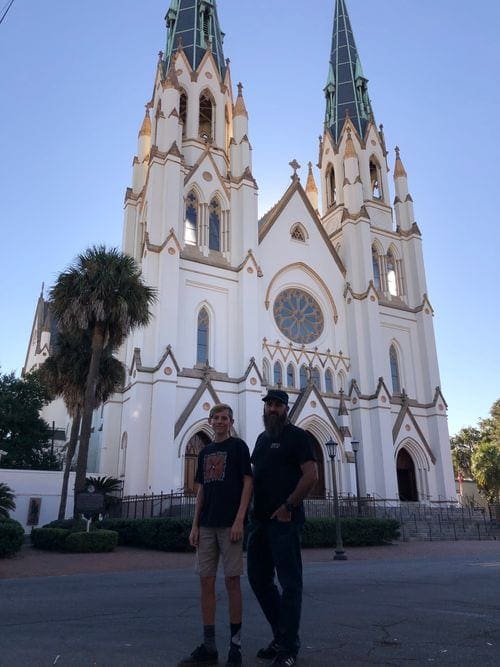 A dad and his teen son stand in front of the towering The Cathedral Basilica of St. John the Baptist.