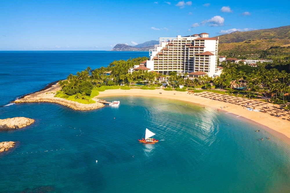An aerial view of Four Seasons Resort Maui at Wailea, featuring a far-reaching shoreline, tall resort buildings, and numerous palm trees.