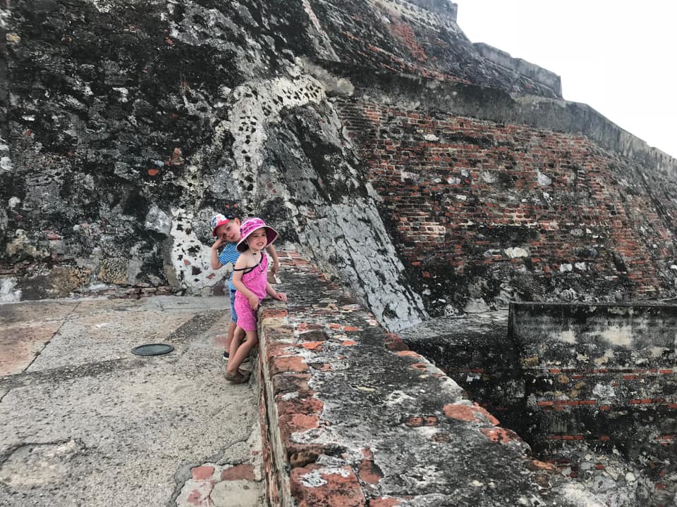 Two kids lean against an ancient wall along the Castillo San Felipe Fortress, one of the best things to do in Cartagena with kids.