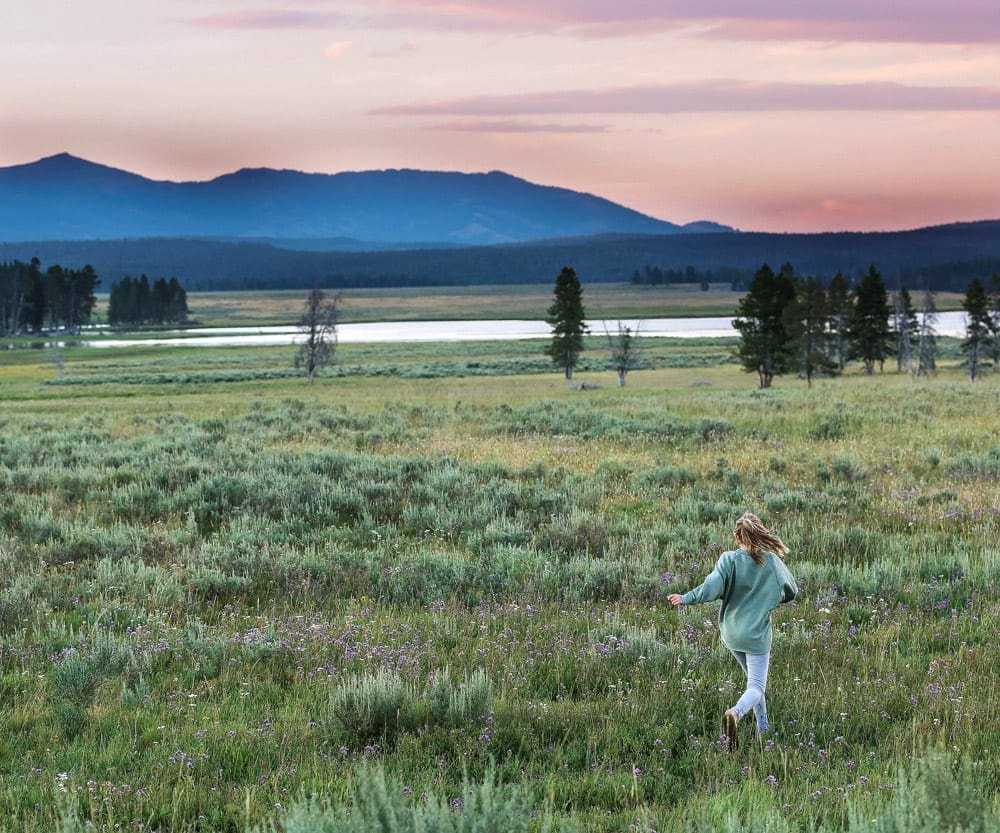 A young girl runs through a field in Yellowstone National Park at dusk.