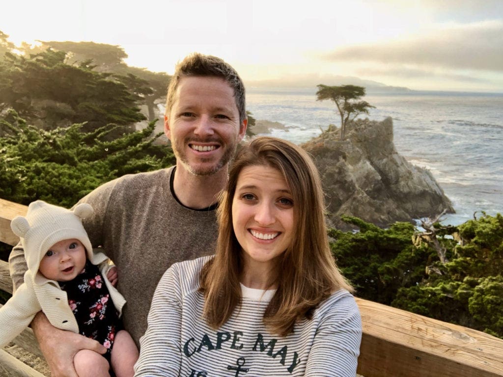 Two parents and a baby in front of a scenic viewpoint in Big Sur, one of the best weekend getaways from San Francisco for families. 