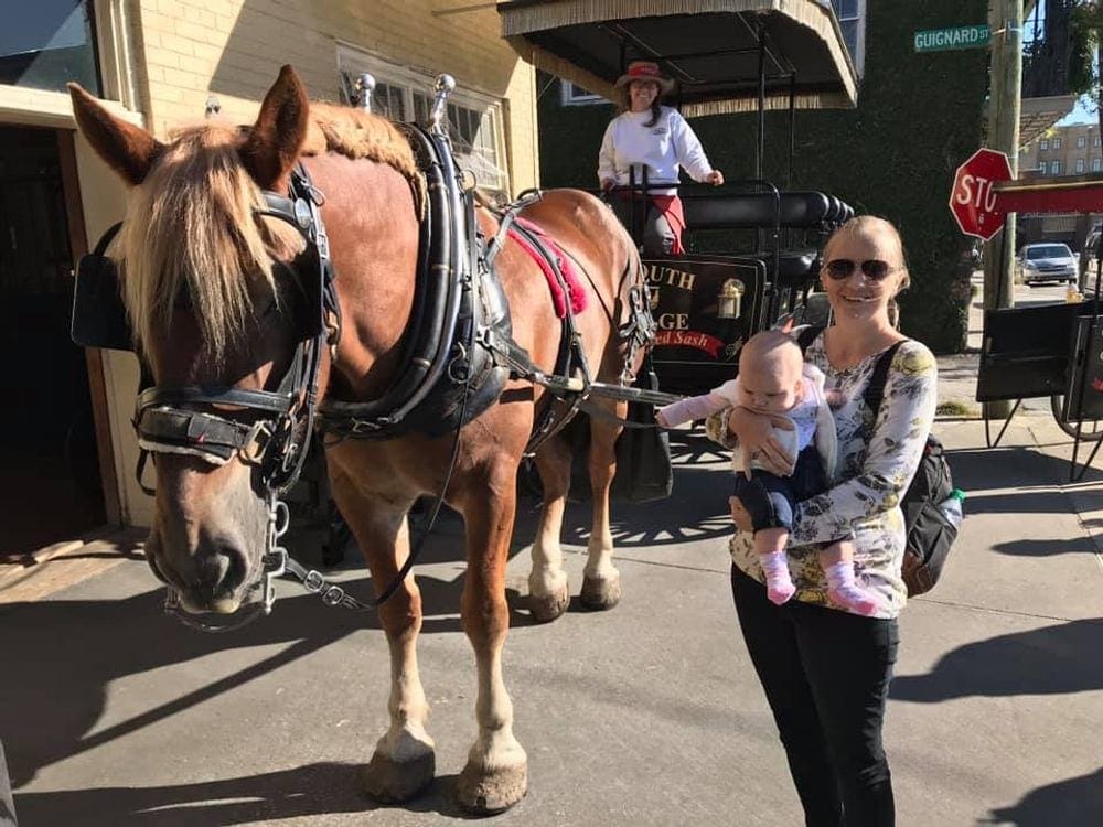 A woman holds a baby near one of the horse-drawn carriages in Charleston.