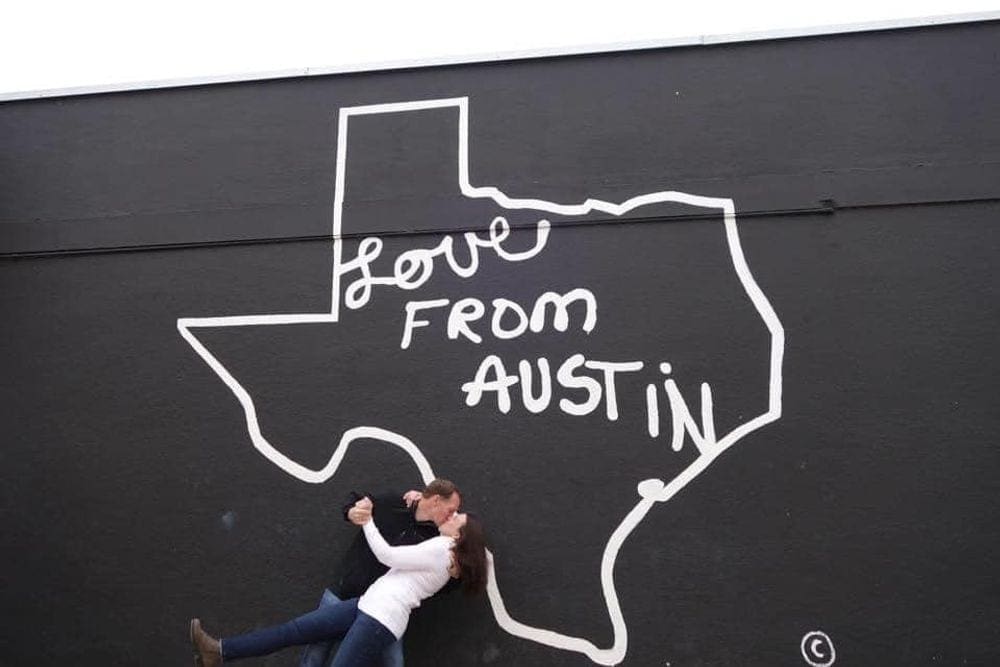 A husband dips his wife for a kiss in front of a sign that reads "Love From Austin".