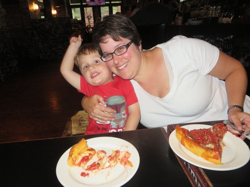 A young boy and his mom smile while enjoying deep dish pizza, one of the best Things To Do Chicago with Kids.