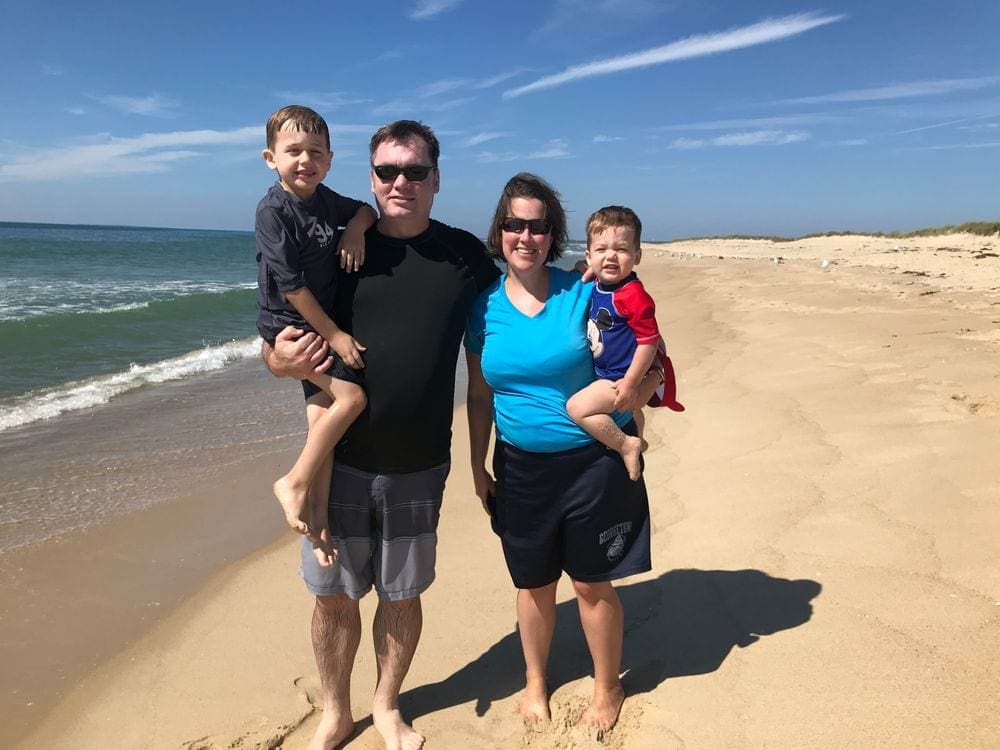 A family of four stands together smiling on a sunny day at Long Point Beach, one of the best things to do on your Family Vacation in Martha's Vineyard.